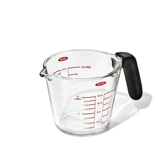 A clear glass measuring cup with red measurement markings and a black handle.