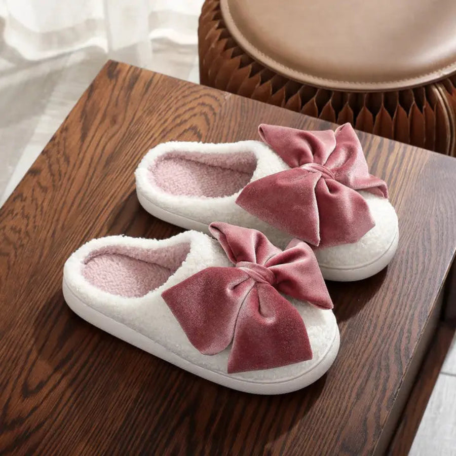 White slippers with pink bows on a wooden surface
