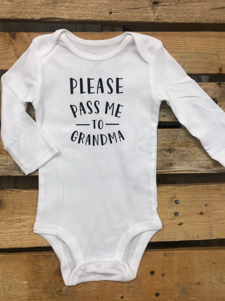 A white long sleeve bodysuit with text printed on the front, placed on a wooden surface.