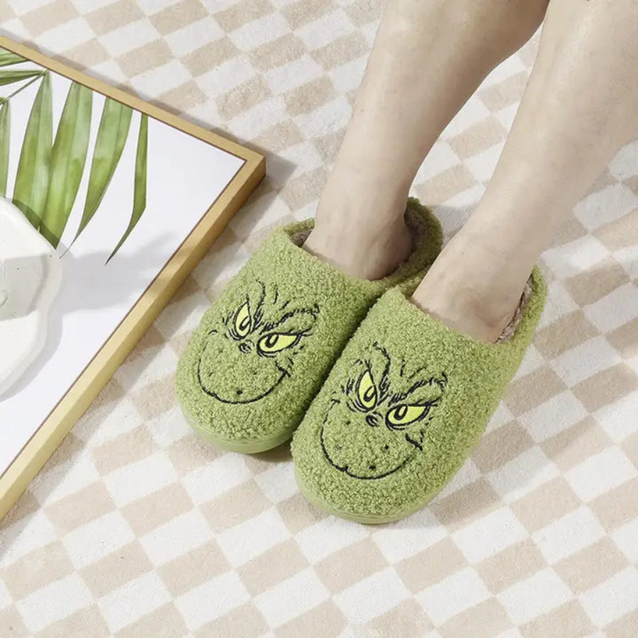 Green slippers with grinch design worn by a person on a checkered floor.