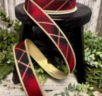 A red and black plaid ribbon with gold trim draped over a small black stool, with green foliage in the background.
