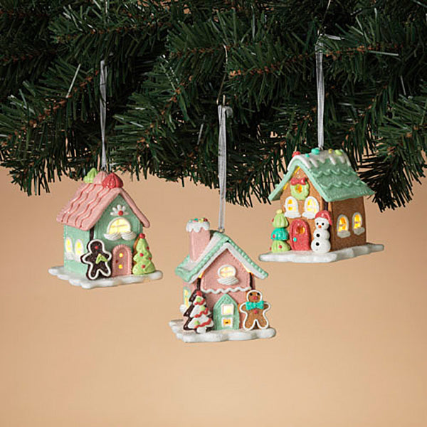 Three lighted clay dough house ornaments with pastel colors and festive decorations, hanging from a Christmas tree.