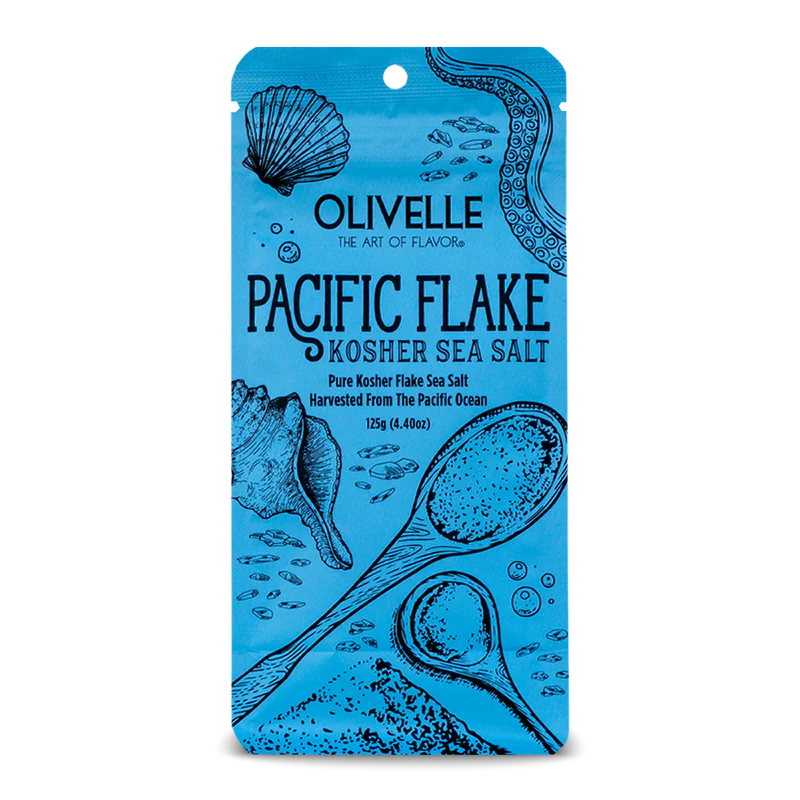 A blue package of Olivelle Pacific Flake Kosher Sea Salt with illustrations of shells and text depicting the product details.