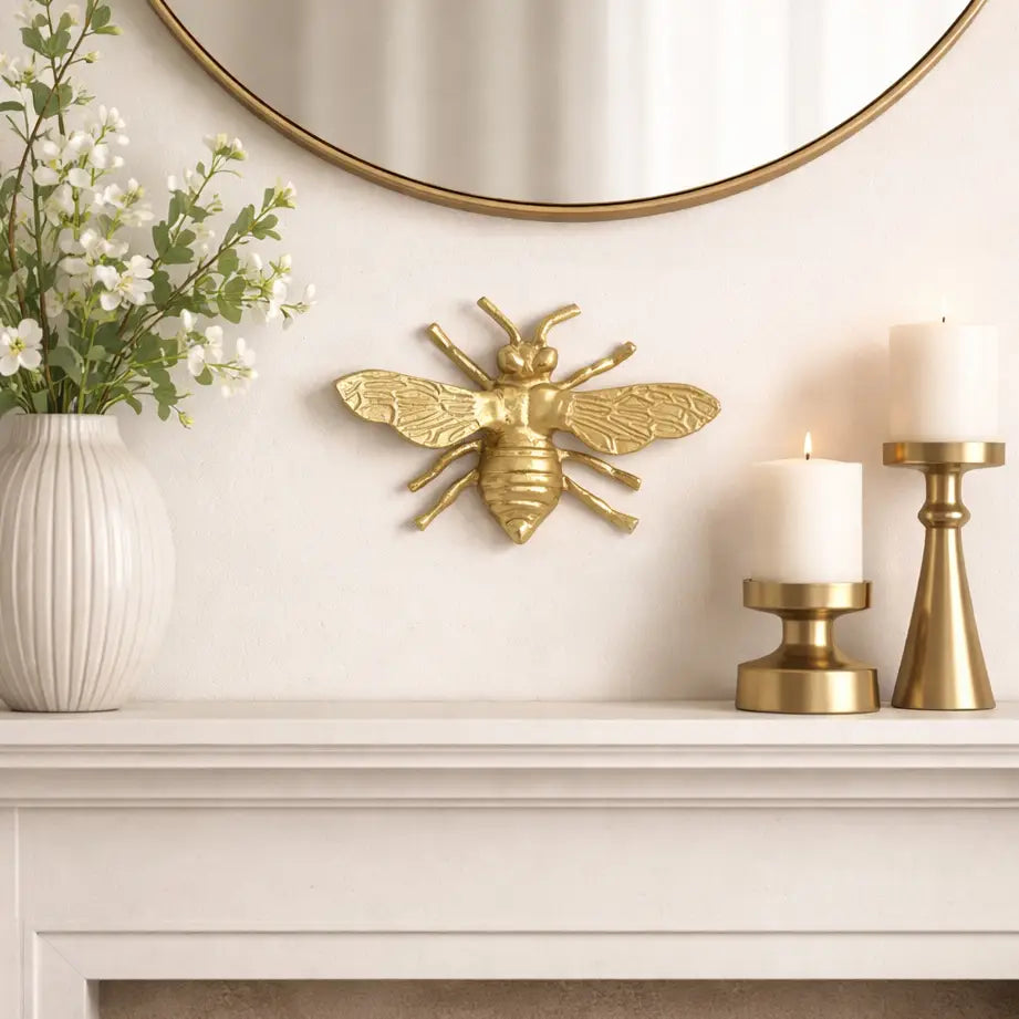 Decorative gold bee on a white mantelpiece with candles and flowers.