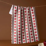 Towel with red apple pattern hanging on a line against a brown background