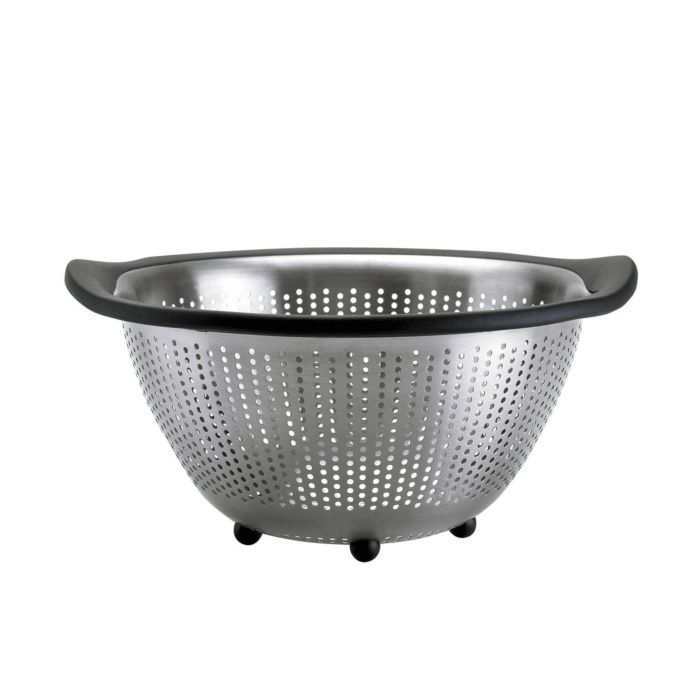 A stainless steel OXO 5QT colander with black handles and feet, featuring a round shape with perforations throughout.