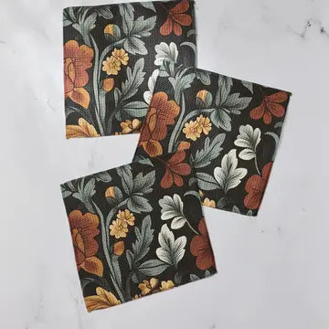Three square fabric napkins with a vintage floral pattern in orange, yellow, and gray on a black background, arranged on a white marble surface.