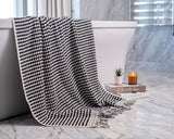 Black and white checkered towel draped over a bathtub with books and a candle on a marble surface.
