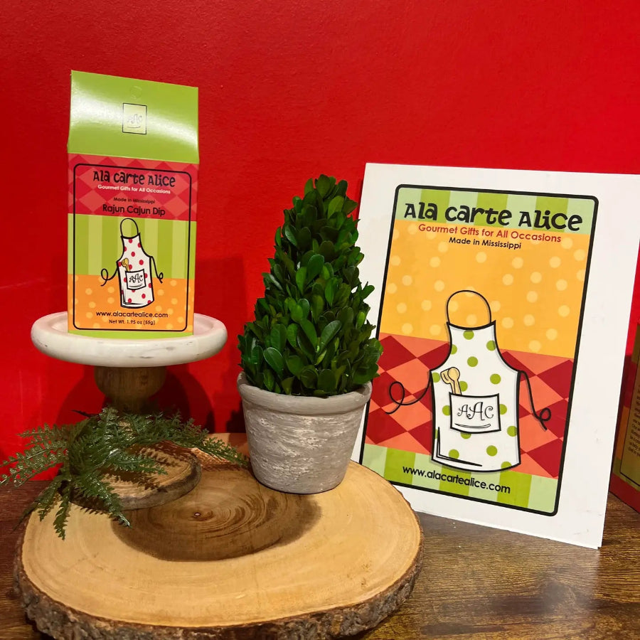 Gourmet gift packaging with a plant and promotional card on a wooden stand against a red background.