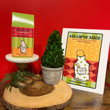 Gourmet gift packaging with a plant and promotional card on a wooden stand against a red background.