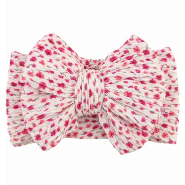 A fabric bow headband with a textured, crinkled material featuring a pink and red floral pattern on a white background, isolated on a white studio background.