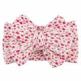 A fabric bow headband with a textured, crinkled material featuring a pink and red floral pattern on a white background, isolated on a white studio background.