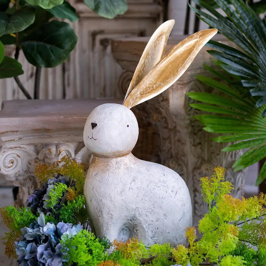 Decorative stone rabbit figure with gold ears in a garden setting