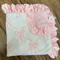 A pink carseat blanket with white bows and a ruffled edge, displayed on a flat surface.