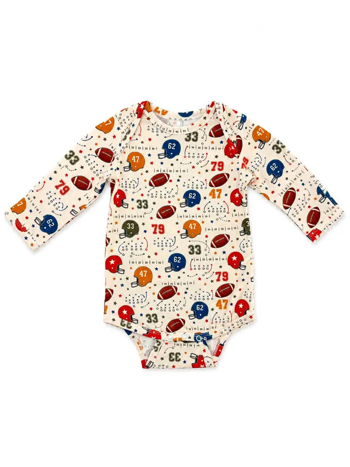 A long-sleeve baby bodysuit with an all-over football-themed print on a cream background, featuring red, blue, and brown footballs, helmets, numbers, and small stars.