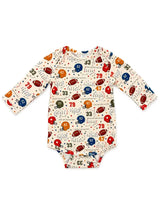 A long-sleeve baby bodysuit with an all-over football-themed print on a cream background, featuring red, blue, and brown footballs, helmets, numbers, and small stars.