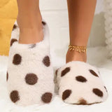 A person wearing fluffy white slip-on slippers with large brown polka dots, shown from the calves down against a soft indoor background.
