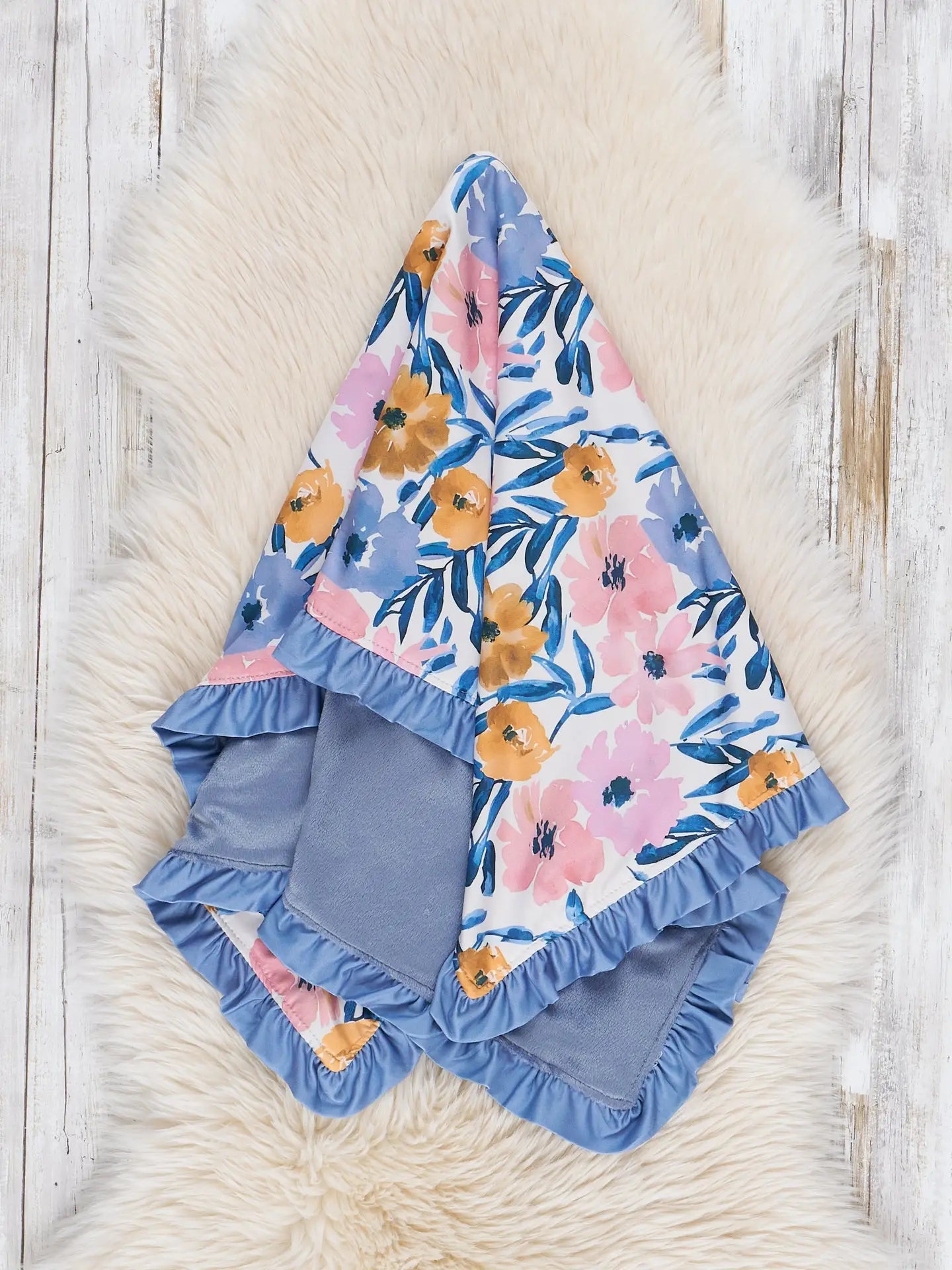 Floral baby blanket with ruffled edges on a wooden surface