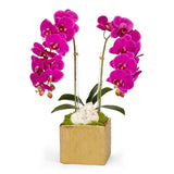 A potted artificial Phalaenopsis orchid arrangement with bright magenta blooms, green leaves, moss, a white decorative stone, and a square gold planter on a light gray background.
