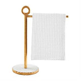 A gold-colored tea towel stand with a white towel hanging on it.