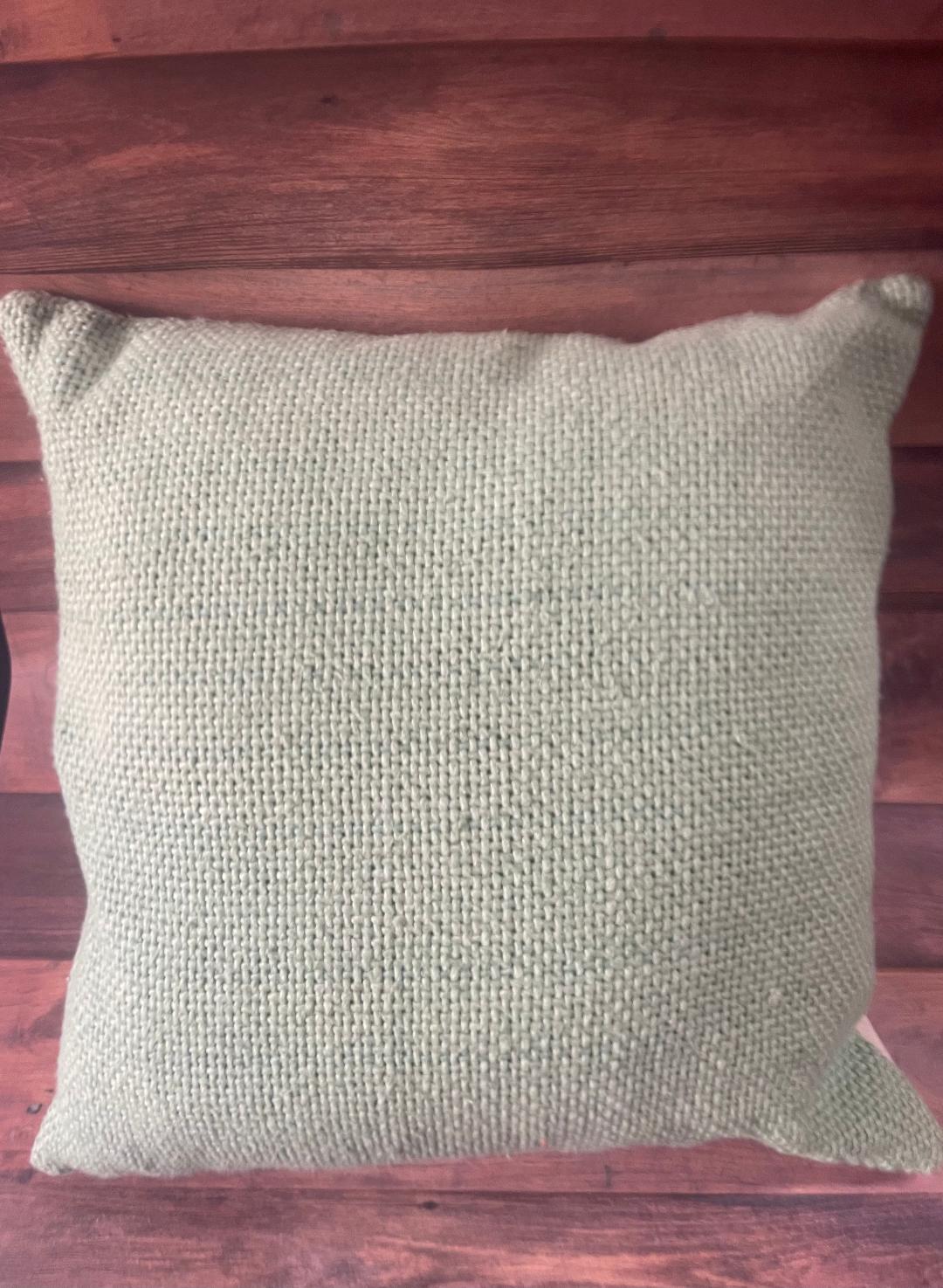 A light green throw pillow with a textured design placed on a wooden surface.