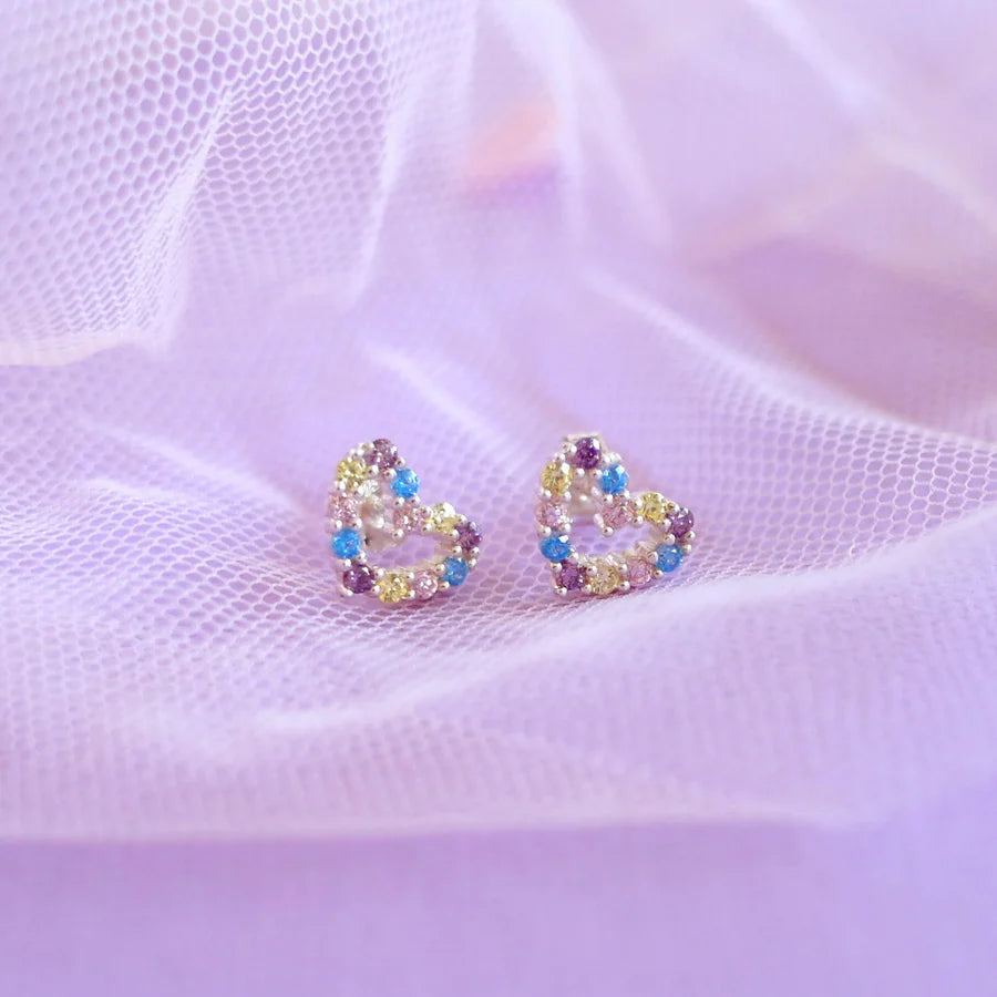 Heart-shaped earrings with colorful stones on a soft purple fabric background