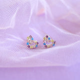 Heart-shaped earrings with colorful stones on a soft purple fabric background