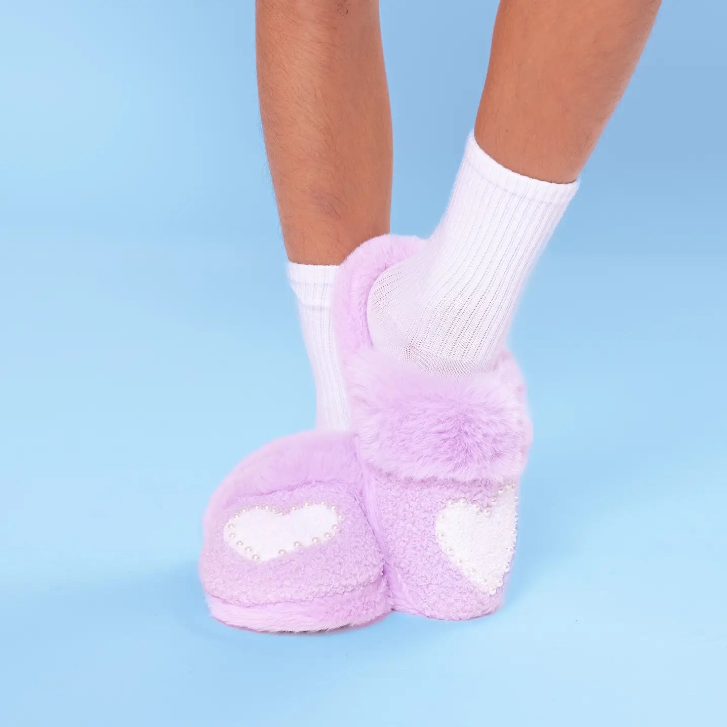 Purple fuzzy socks with white hearts worn by a person on a light blue background
