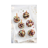 Dessert balls with cranberries and nuts on skewers on a white surface.