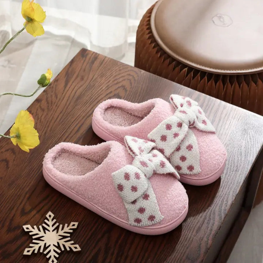 Pink slippers with white bows on a wooden surface with yellow flowers and a snowflake decoration.