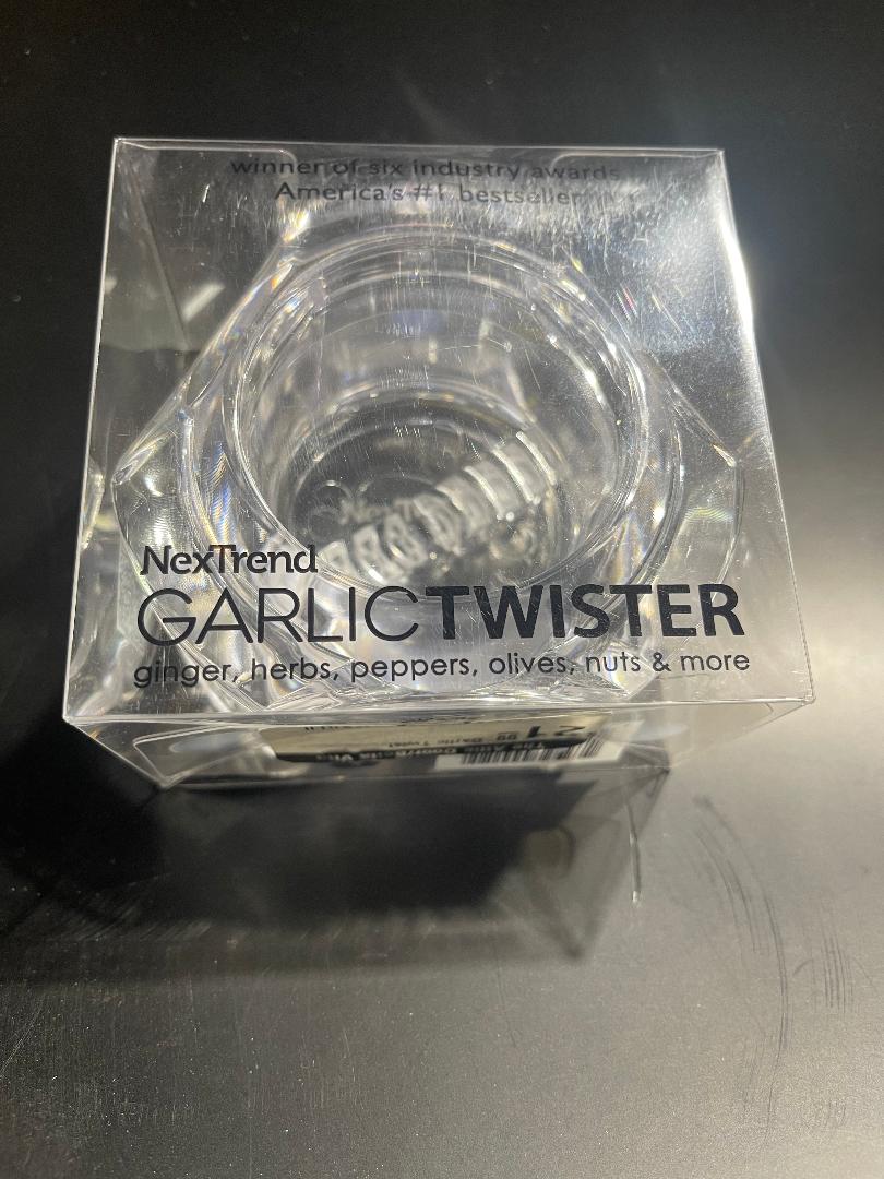 A clear, plastic garlic twist tool with a twisting mechanism, branded by NexTrend, intended for mincing garlic and other kitchen tasks.