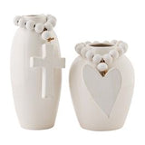 Two white stoneware vases with cross and heart designs, adorned with beads.