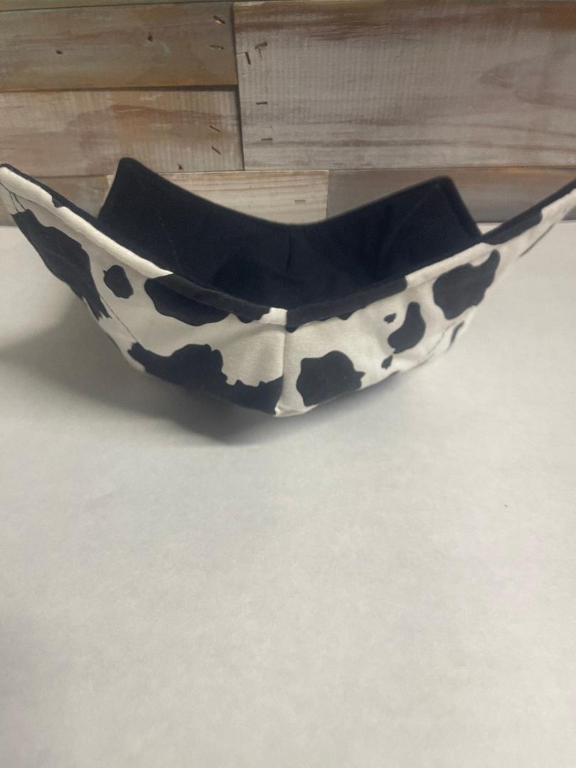 A black and white cow print cozy bowl hot pad designed to fit around a bowl for handling.