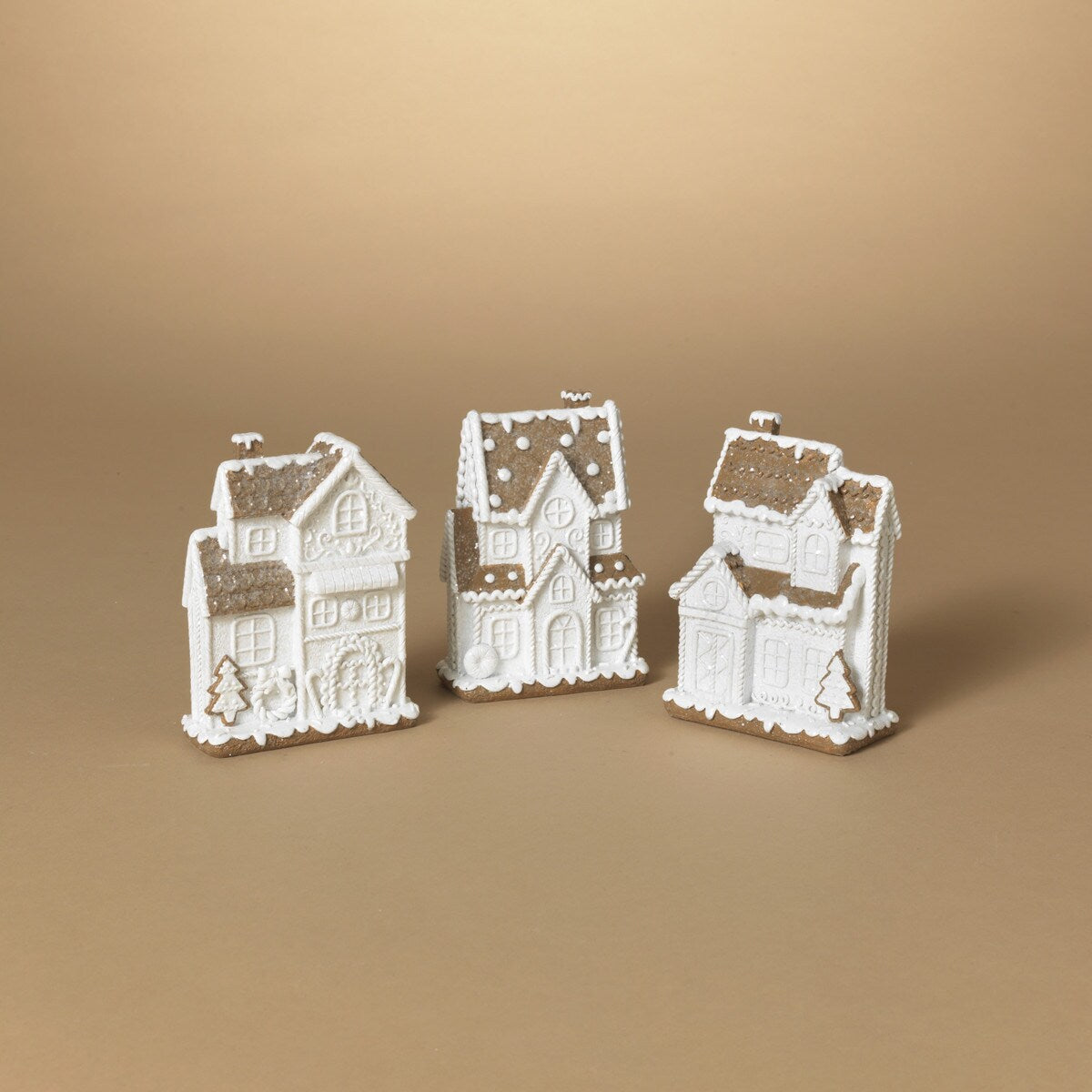 This image displays a set of three intricately designed Resin Gingerbread Houses, positioned against a neutral beige background. Each house is crafted from white resin, featuring detailed architectural elements that include arched windows, decorative molding, and sloped roofs, highlighted with darker shading to enhance the three-dimensional effect.