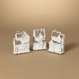 This image displays a set of three intricately designed Resin Gingerbread Houses, positioned against a neutral beige background. Each house is crafted from white resin, featuring detailed architectural elements that include arched windows, decorative molding, and sloped roofs, highlighted with darker shading to enhance the three-dimensional effect.