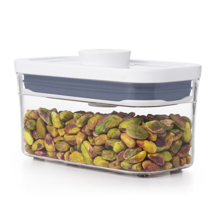 A clear plastic OXO pop container filled with pistachios, featuring a white and grey lid.
