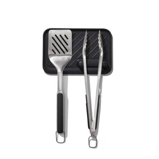 A grilling set consisting of a flat spatula, a basting brush, and a pair of tongs, all with stainless steel handles and black accents, displayed on a white background.