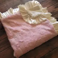 A pink and cream colored car seat blanket with a ruffled edge, laid out on a wooden floor.