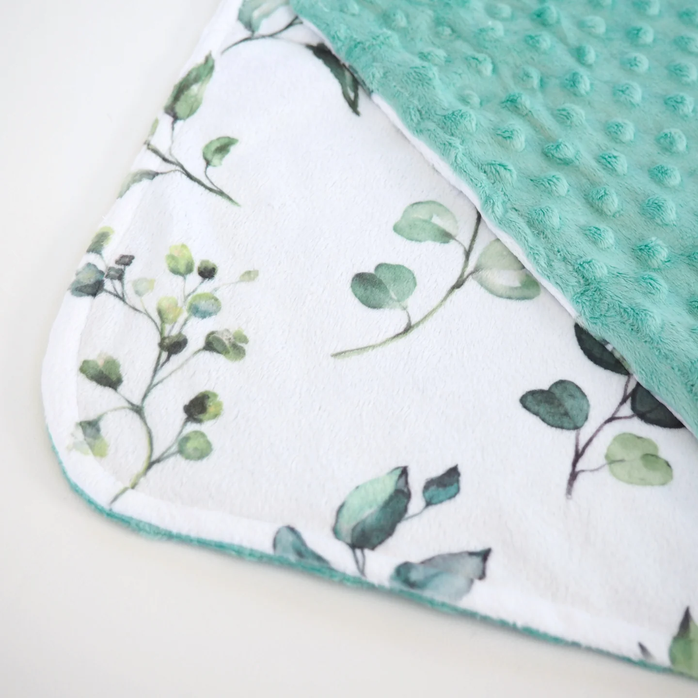 A plush baby blanket with a farm animal theme, featuring characters such as cows, pigs, and chickens, and a red barn.