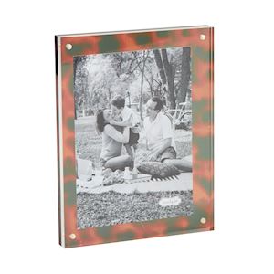 A picture frame with a tortoise shell-like pattern, displaying an old photograph of two individuals sitting close by a lake.