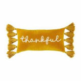 A rectangular velvet throw pillow with the word 'blessed' written on it, adorned with tassels on the sides.