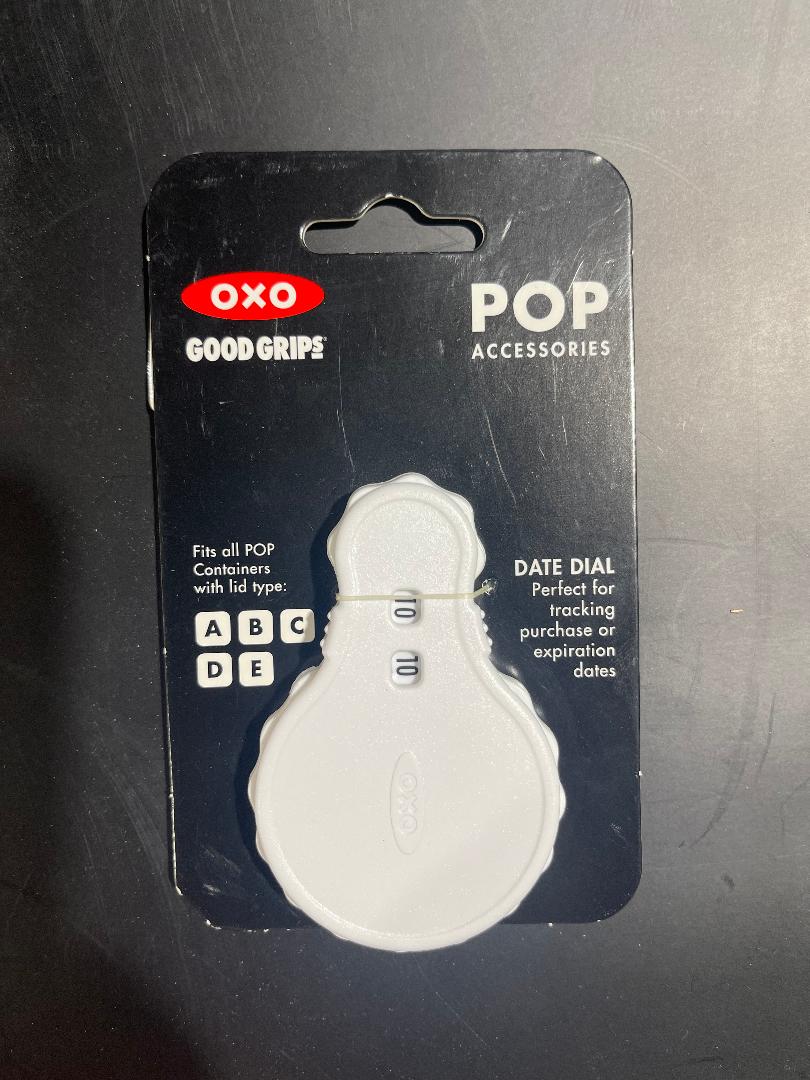 An OXO Good Grips POP container dial accessory, packaged on a black background with product information.