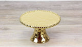 A gold-colored pedestal cupcake stand with a textured top surface and decorative feet.