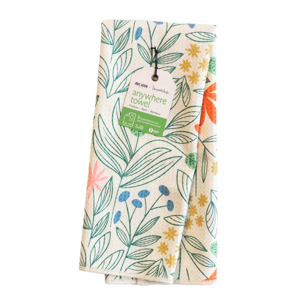 An oversized kitchen towel with a leaf and floral pattern, made from recycled fabric, with a hanging loop on one corner.