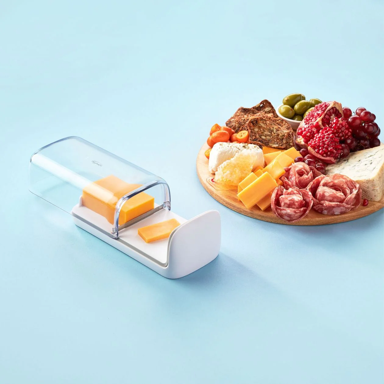 A cheese storage box with a white body and orange lining, displayed alongside a platter of various cheeses and meats.