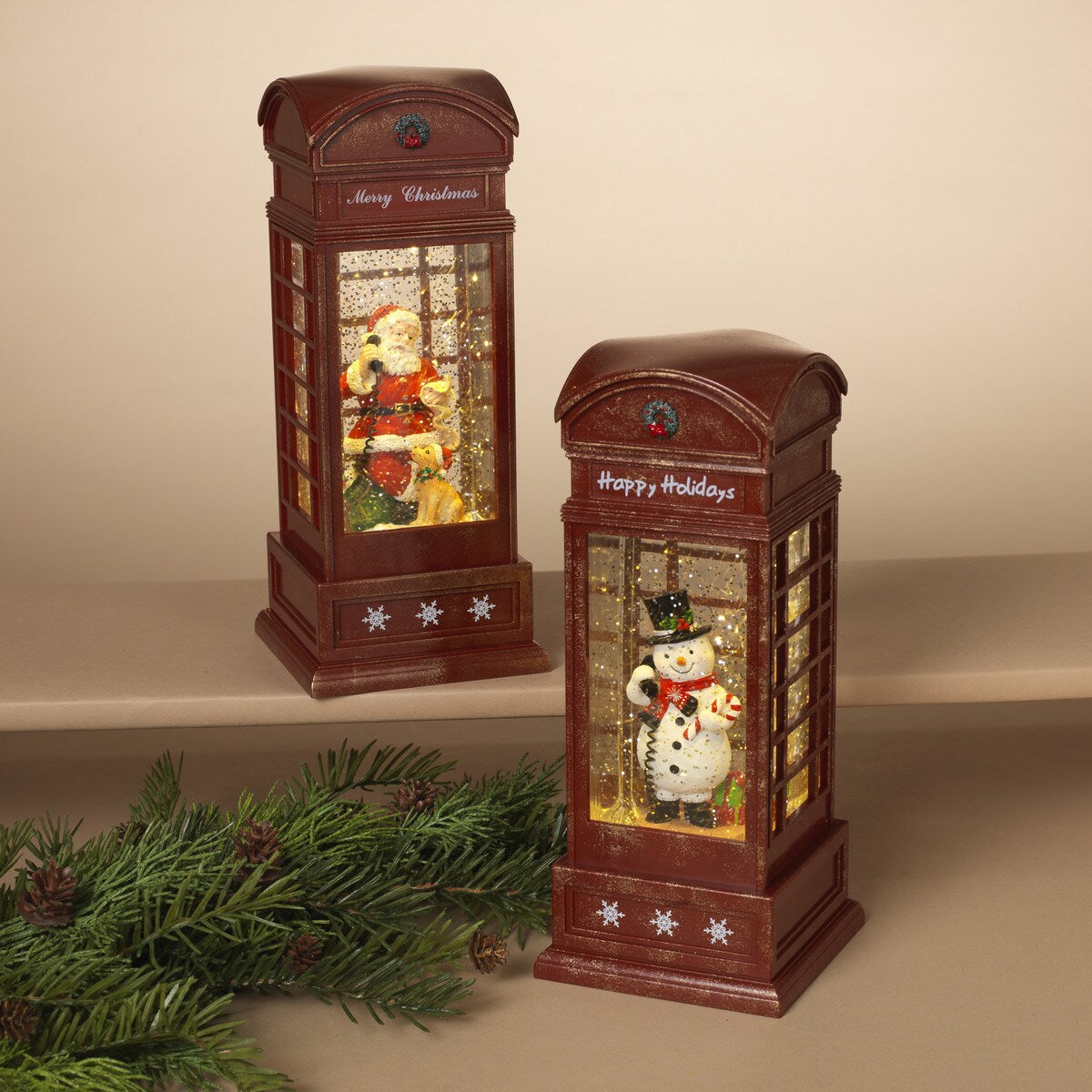 Two decorative spinning telephone booth globes with holiday-themed figures inside, placed on a surface with festive decorations.