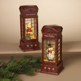 Two decorative spinning telephone booth globes with holiday-themed figures inside, placed on a surface with festive decorations.