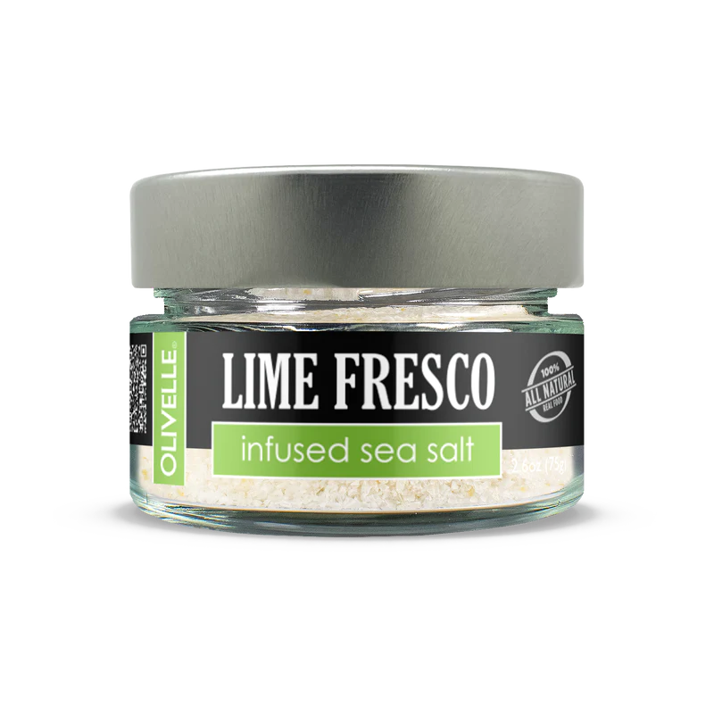 A clear glass jar containing infused sea salt with a label that reads 'Lime Fresco' and 'Olivelle'. The jar has a metallic lid and is presented against a white background.
