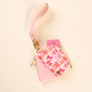 A wristlet pouch with a pink exterior featuring a blushing bows print, a detachable strap, and metal hardware.