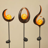 A set of three outdoor solar stake lights with a metallic design and a glowing orange globe at the top, mounted on a black stake.